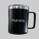 Black mug with 'Humana' branding on a white surface with a wooden background